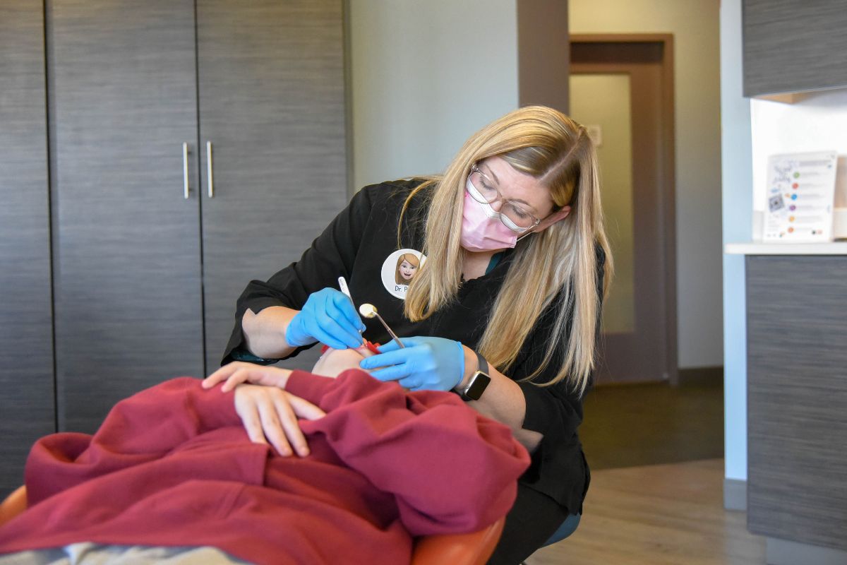 Orthodontic provider wearing gloves and a mask while performing a dental procedure on a patient in a modern treatment room